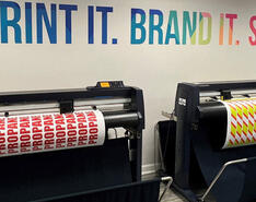A printing machine is displayed printing off signs and marketing material.