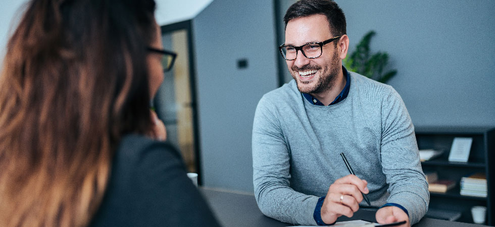 A man interviews a woman in an office setting.