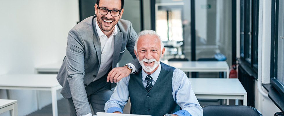 A father and son are pictured in an office smiling at the camera.