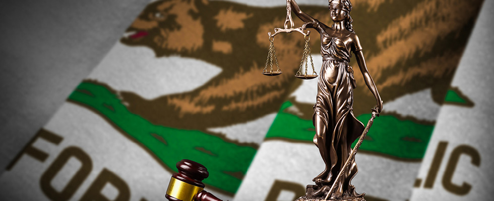 A statue of lady justice is pictured in front of the California state flag.