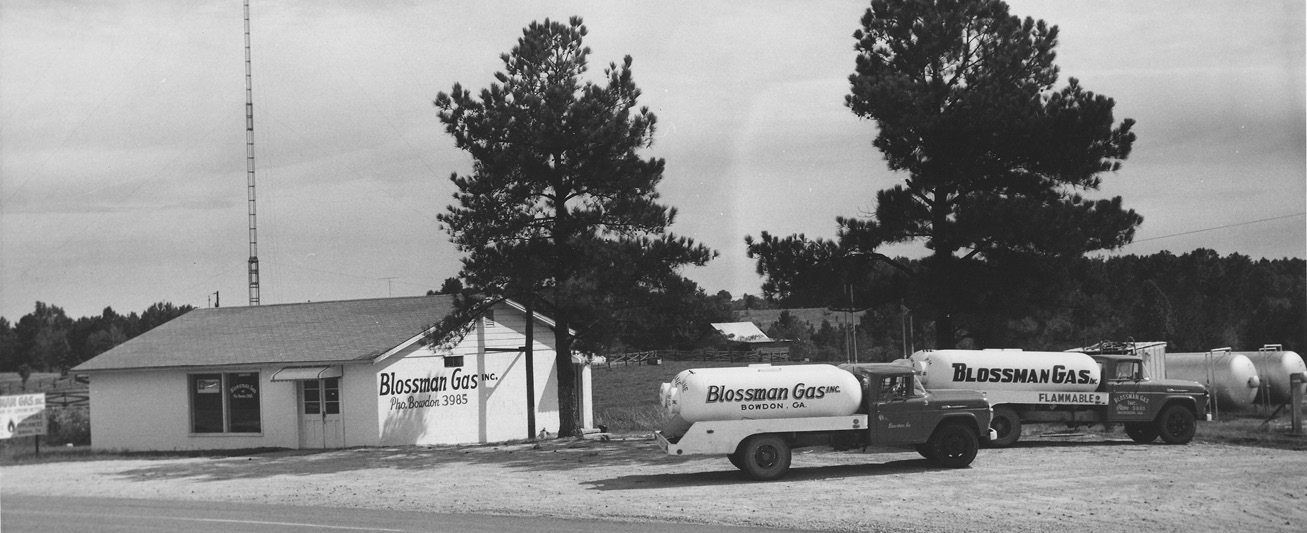 A black-and-white photo shows the old office building and several trucks of Blossman Gas.
