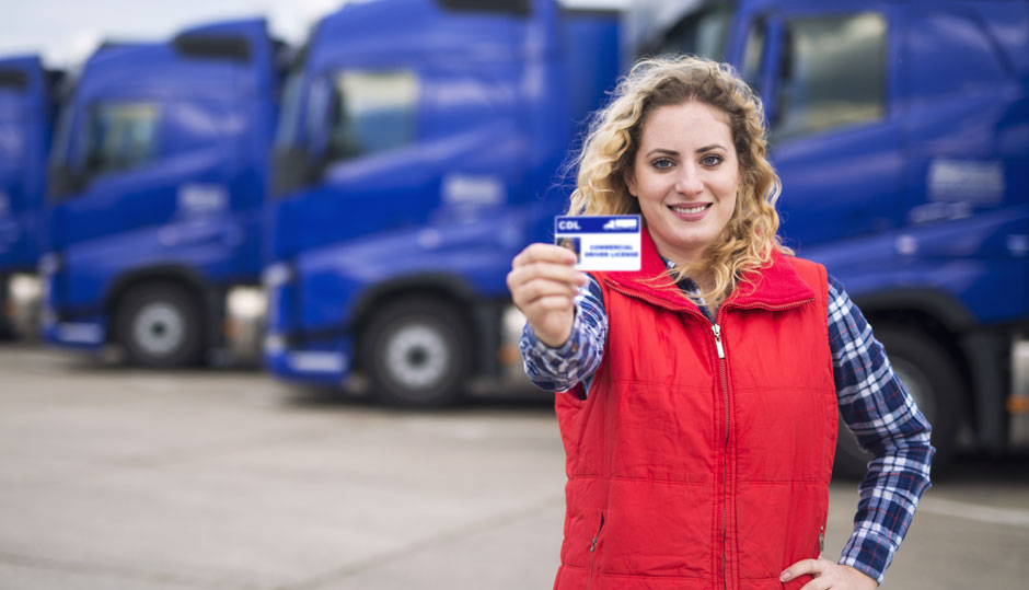 A woman standing in front of a row of transport trucks holding up a CDL license