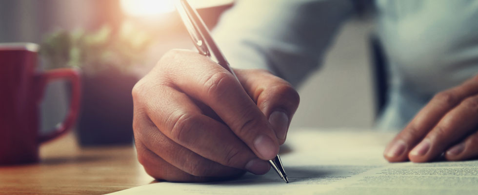 A person's hand holding a pen and writing a letter