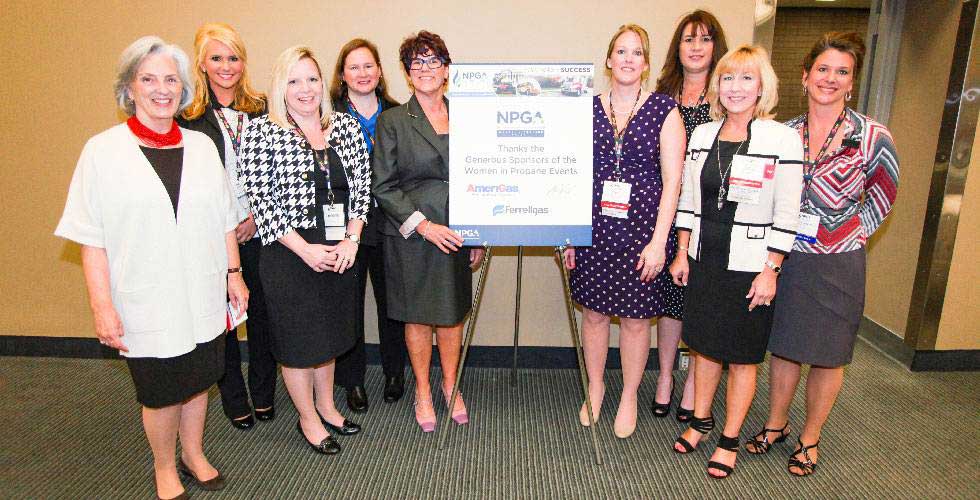 Nine Womon in Propane Council members stand around an NPGA event sign at a roundtable session in Atlanta, Georgia, in 2014. All of the women pictured were volunteer leaders on various levels within the organization.